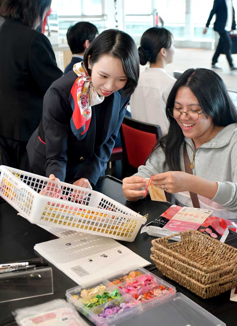 水引を装飾したスーツケースタグの制作体験を楽しむ旅客(右)=成田市の成田空港